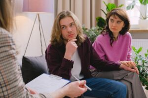 Two individuals participating in a counseling session, seated together and speaking with a therapist.